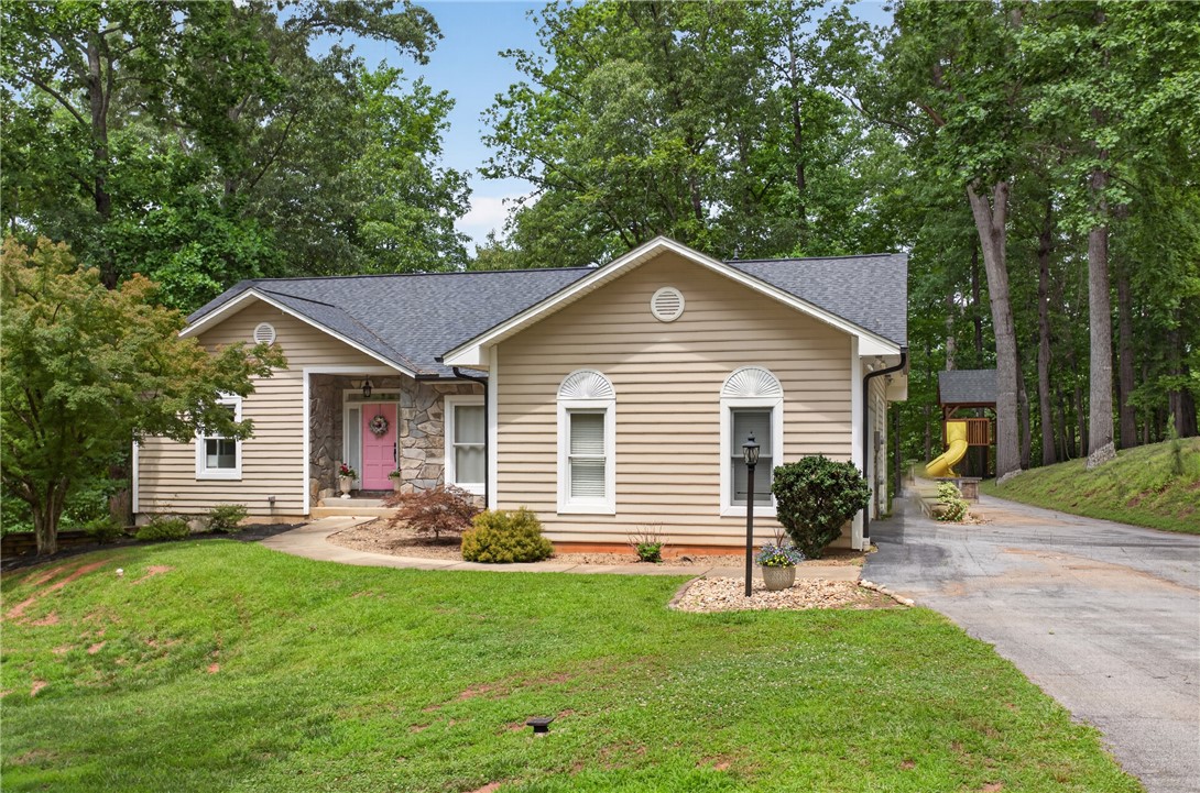 136 Loran Pointe Circle Seneca, SC 29672 - Photo 2 of 50 A charming single-story residence with a welcoming pink front door, nestled amidst lush greenery and mature trees.