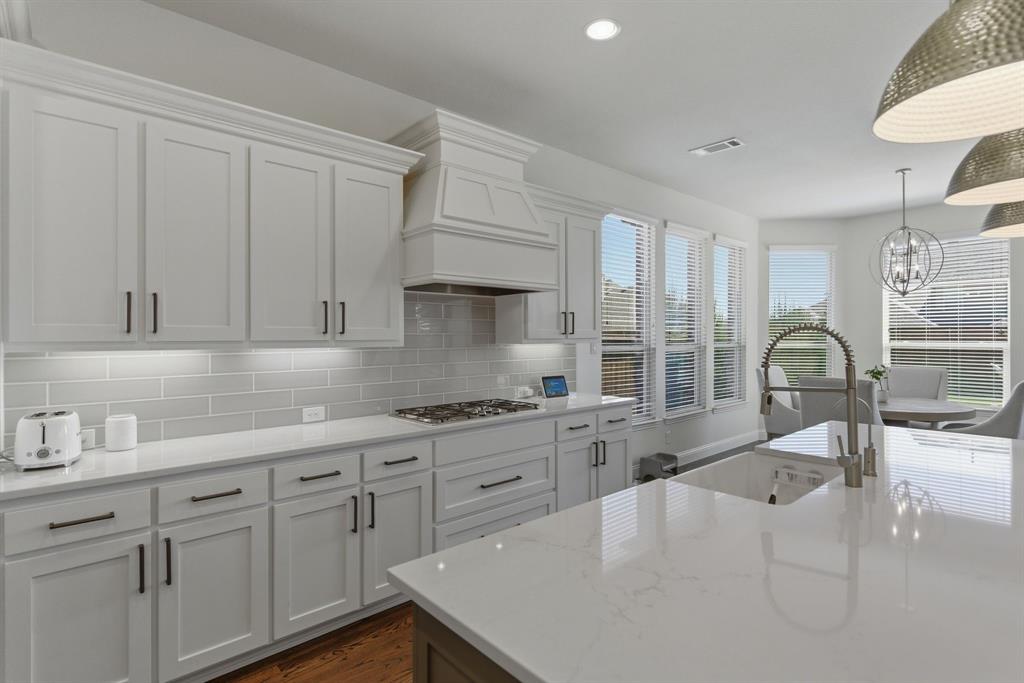 2801 Seabiscuit Road Celina, TX 75009 - Photo 10 of 39 Kitchen featuring white cabinets, light stone counters, a chandelier, dark wood-type flooring, and decorative backsplash