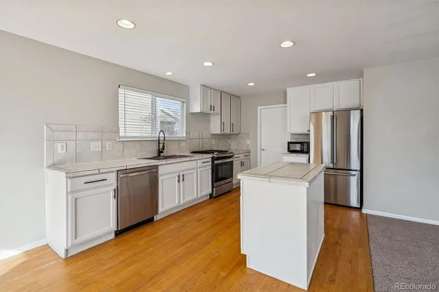 a kitchen with a refrigerator a sink dishwasher a stove top oven a refrigerator with white cabinets and wooden floor