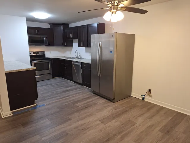 a kitchen with stainless steel appliances granite countertop a refrigerator a sink dishwasher a stove with wooden cabinets and floor