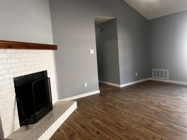 a view of an empty room with wooden floor and a fireplace