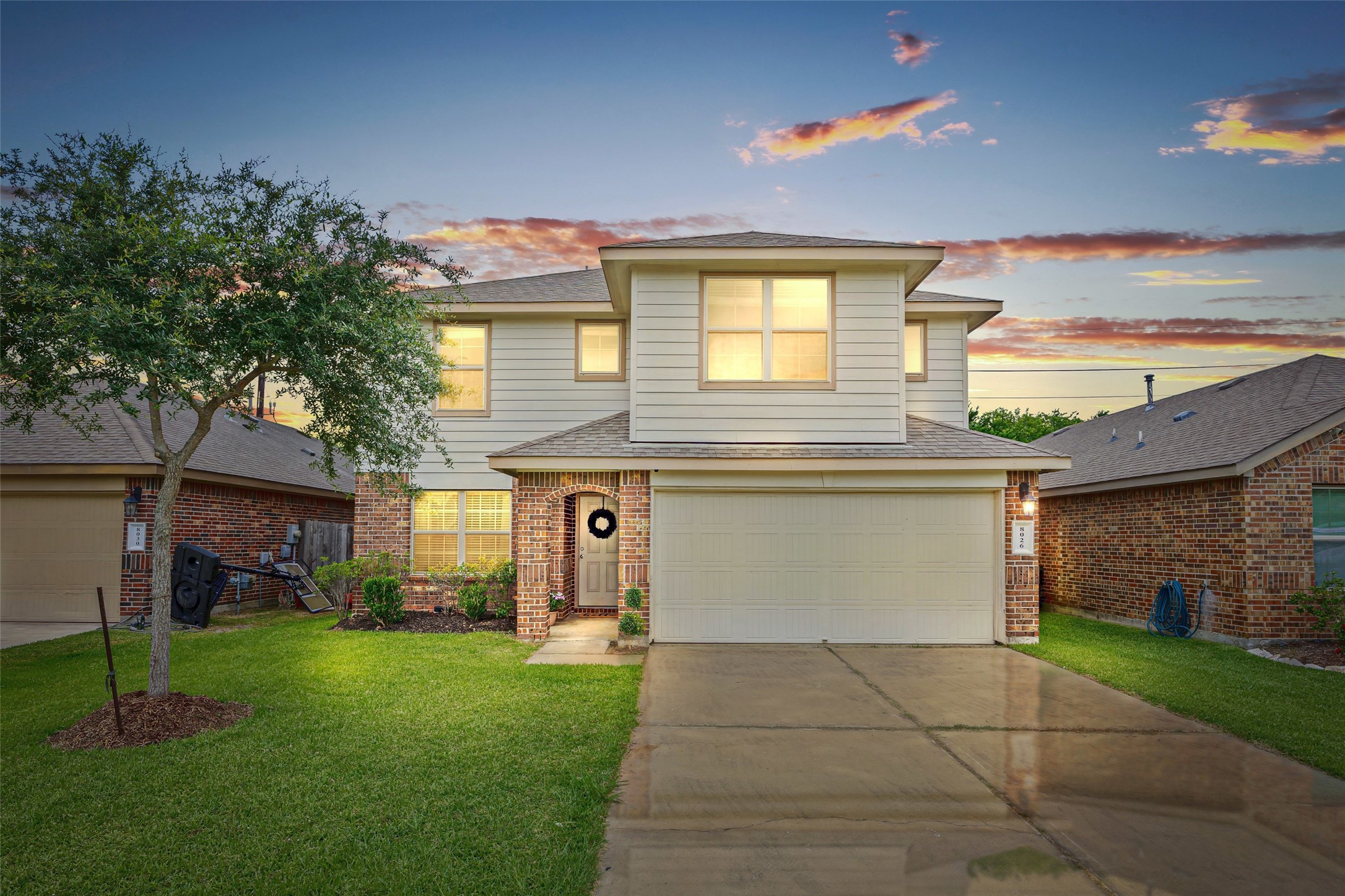 8026 Farthing Lane Rosharon, TX 77583 - Photo 1 of 13 This two-story home features a modern facade with a combination of brick and siding. It includes a neatly manicured lawn, a two-car garage, and a welcoming front entrance. The property is set against a picturesque sunset backdrop, creating a warm and inviting atmosphere.