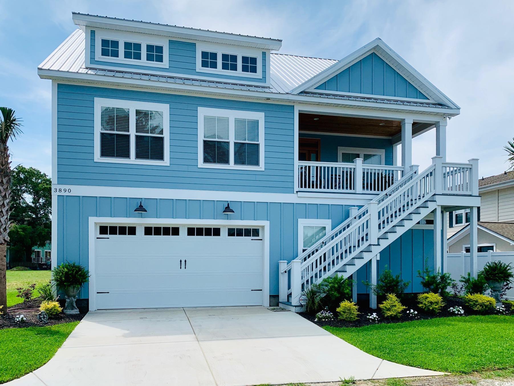 Beach home featuring a front lawn, board and batten siding, an attached garage, concrete driveway, and a metal roof