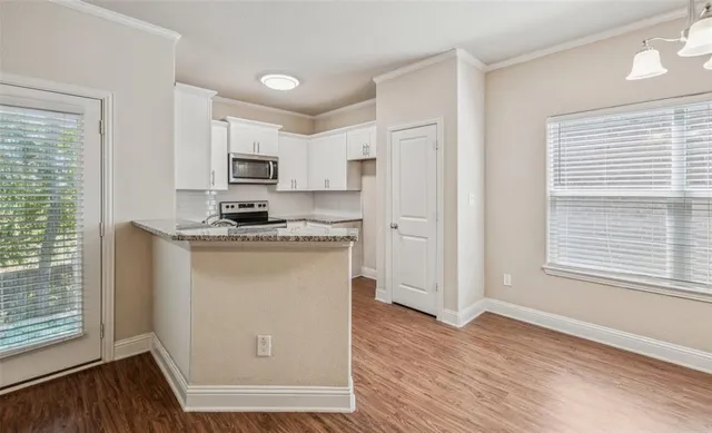 a kitchen with stainless steel appliances granite countertop a refrigerator a stove a sink and white cabinets with wooden floor