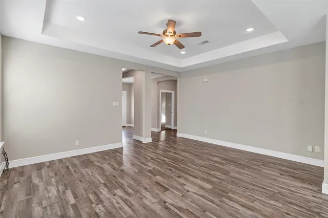 a view of an empty room with wooden floor and a ceiling fan