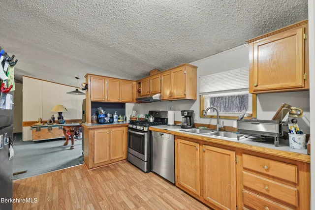 a kitchen with stainless steel appliances granite countertop a refrigerator a sink dishwasher a stove and white countertops with wooden floor