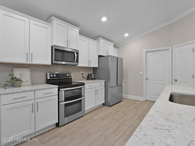 a kitchen with stainless steel appliances granite countertop a refrigerator a stove a sink and white cabinets