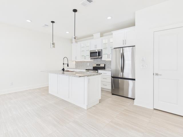 511 Richardson Street Athens, TX 75751 - Photo 9 of 40 Kitchen with appliances with stainless steel finishes, decorative light fixtures, white cabinetry, a center island with sink, and light stone counters