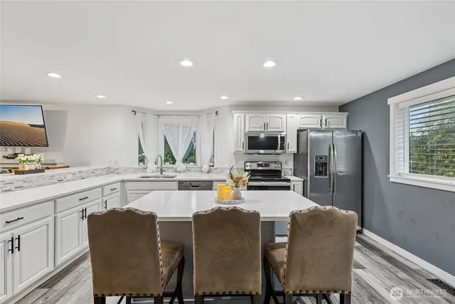 a kitchen with stainless steel appliances granite countertop a dining table chairs refrigerator and microwave
