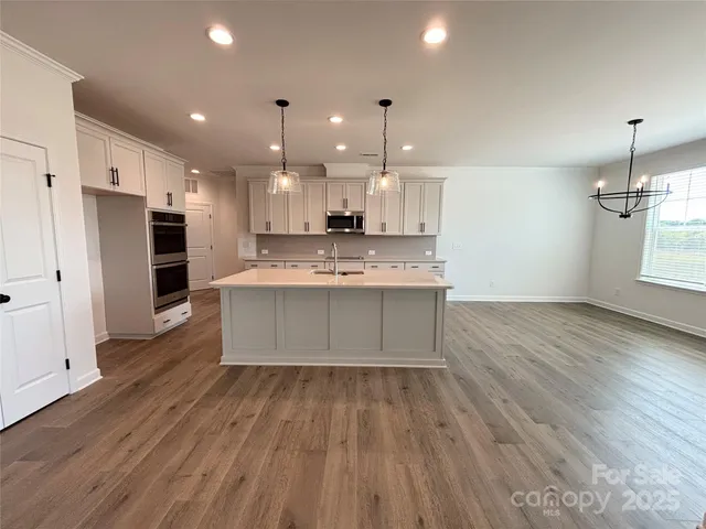 a large kitchen with stainless steel appliances a large counter top a sink dishwasher and a refrigerator with wooden floor