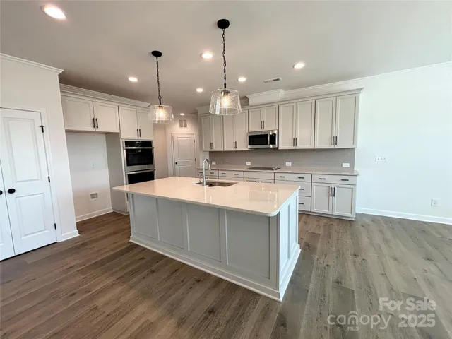 a large kitchen with stainless steel appliances kitchen island granite countertop a stove a sink a refrigerator and white cabinets with wooden floor