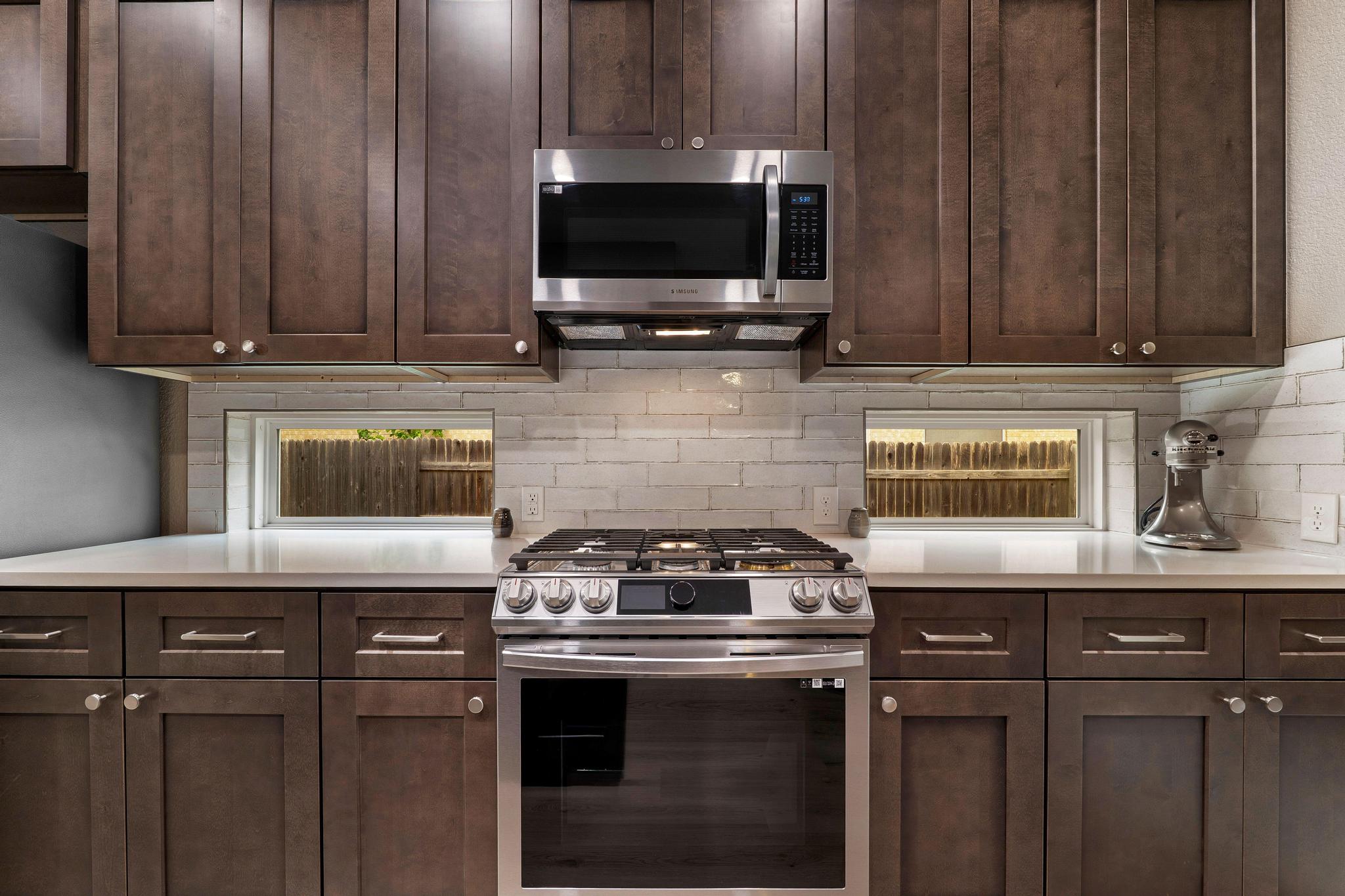 13231 Armaga Springs Road Austin, TX 78727 - Photo 11 of 36 Kitchen featuring stainless steel appliances, dark wood finish cabinetry, tasteful backsplash, and light stone countertops