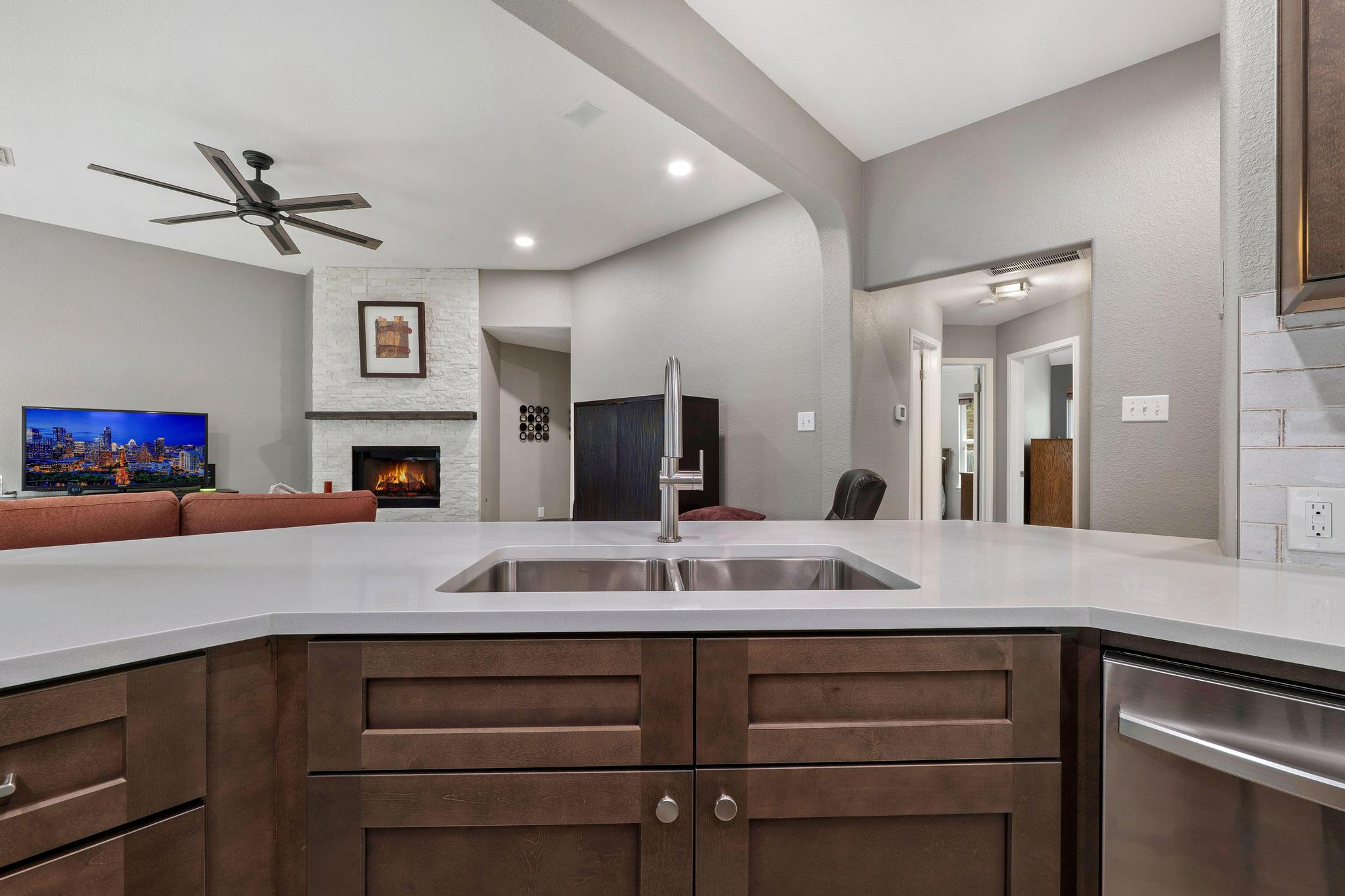 13231 Armaga Springs Road Austin, TX 78727 - Photo 35 of 36 Kitchen featuring open floor plan, a large fireplace, dishwasher, a ceiling fan, and dark wood finish cabinetry
