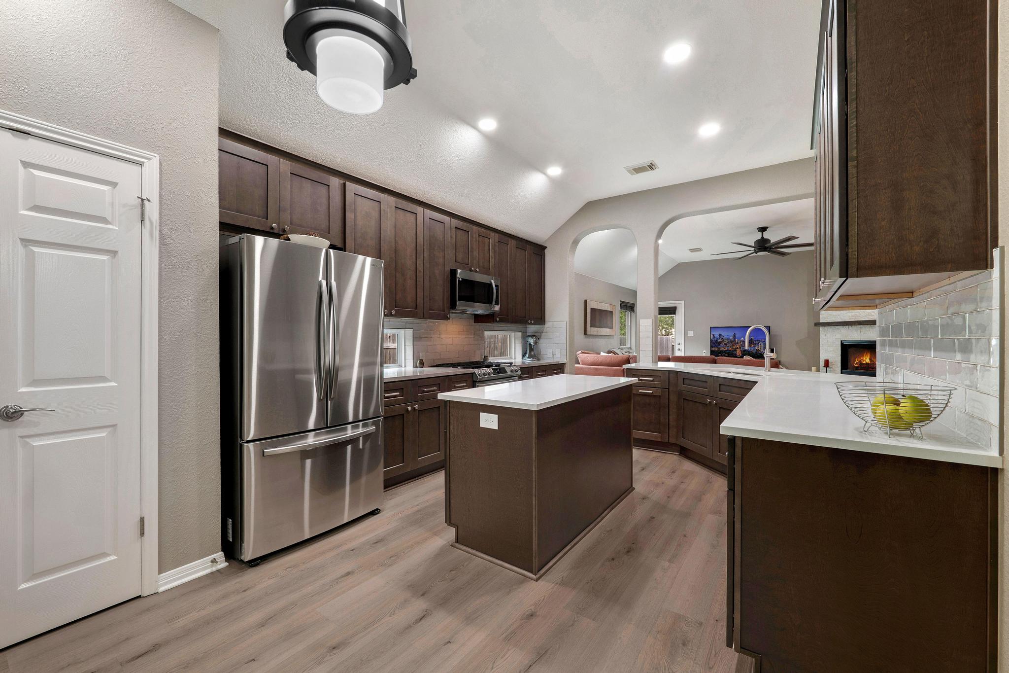 13231 Armaga Springs Road Austin, TX 78727 - Photo 12 of 36 Kitchen with dark wood finish cabinets, a center island, stainless steel appliances, vaulted ceiling, and a peninsula