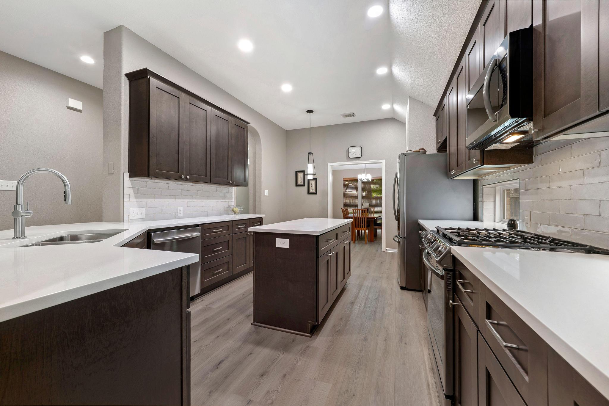 13231 Armaga Springs Road Austin, TX 78727 - Photo 10 of 36 Kitchen with stainless steel appliances, a kitchen island, dark wood finish cabinetry, and light wood finished floors