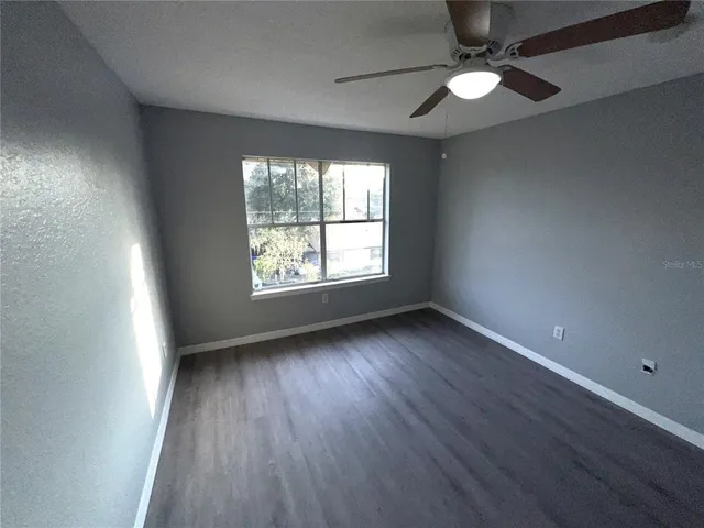 an empty room with wooden floor chandelier fan and windows