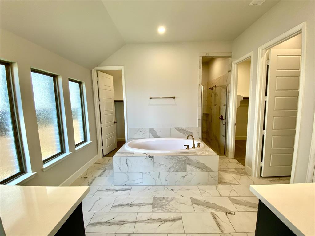 1937 Halkin Road Celina, TX 75009 - Photo 10 of 20 Soaking tub with a tiled surround, patterned floor tiles, multiple privacy windows, a glass-enclosed shower, and built-in cabinetry