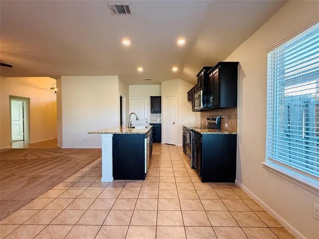 a kitchen with stainless steel appliances kitchen island granite countertop a refrigerator and a view of living room