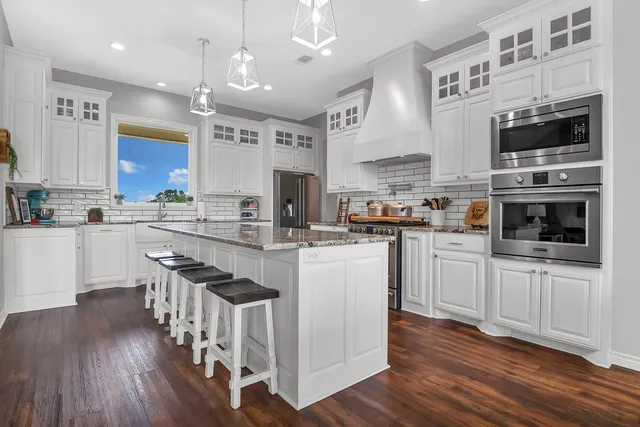 a kitchen with stainless steel appliances granite countertop a stove top oven a sink dishwasher and white cabinets with wooden floor