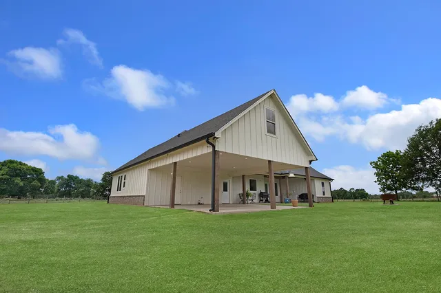 a view of a white house in front of a big yard with plants and large trees