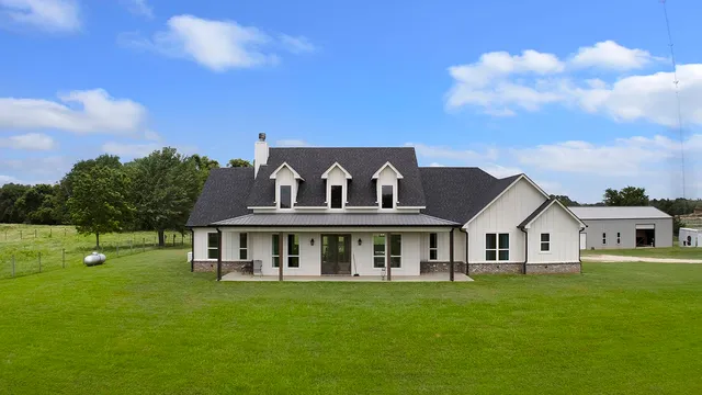 a view of a white house with a big yard and large trees