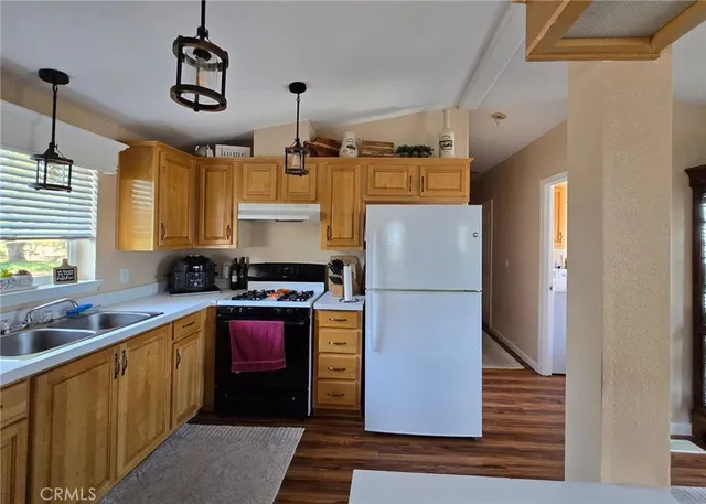 a kitchen with stainless steel appliances granite countertop a refrigerator a sink dishwasher a stove and a dining table with wooden floor