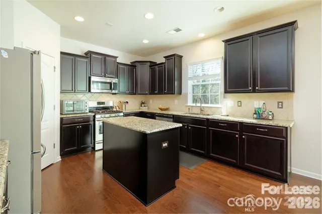 a kitchen with kitchen island granite countertop a sink cabinets and stainless steel appliances