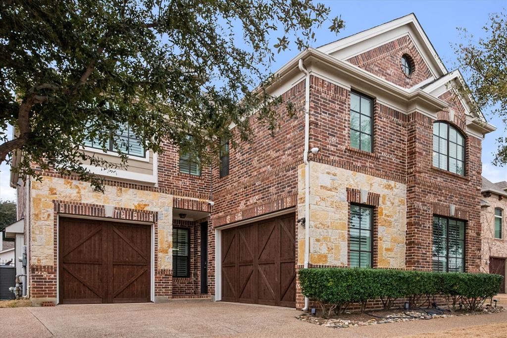 View of front facade featuring a garage, brick siding, driveway, and stone siding