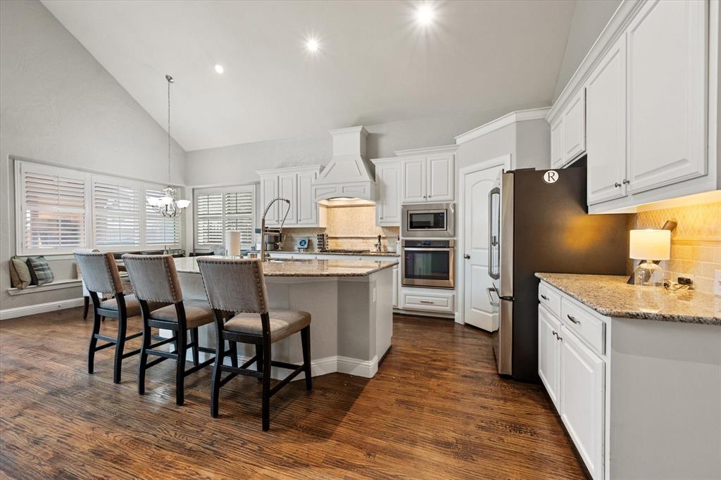 6713 Matador Ranch Road North Richland Hills, TX 76182 - Photo 9 of 39 Kitchen with light stone countertops, lofted ceiling, stainless steel appliances, decorative backsplash, and a breakfast bar area