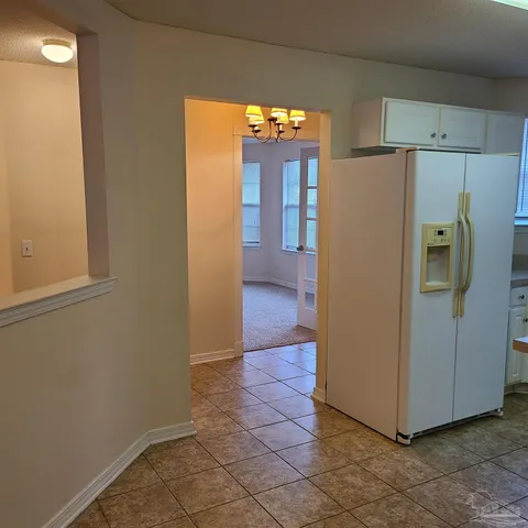 a view of a refrigerator in kitchen and an empty room with wooden floor windows