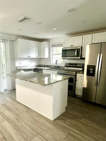 a kitchen with stainless steel appliances granite countertop a stove top oven a refrigerator a sink and dishwasher a oven with wooden floors