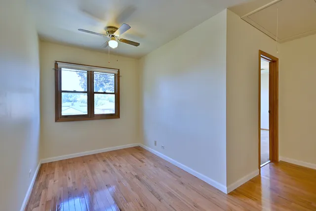 an empty room with wooden floor chandelier fan and windows