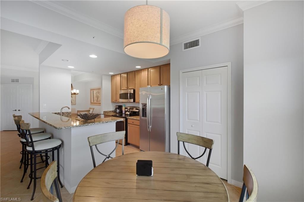 9844 Venezia Circle, Unit 714 Naples, FL 34113 - Photo 18 of 50 a kitchen with stainless steel appliances kitchen island granite countertop a refrigerator a stove a microwave oven a dining table and chairs with wooden floor