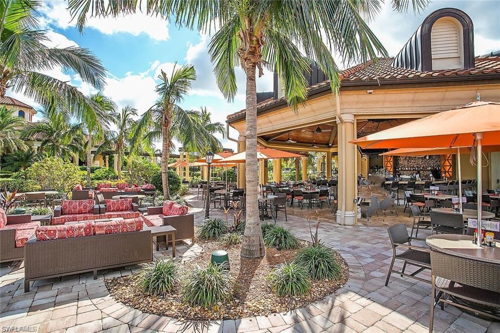9844 Venezia Circle, Unit 714 Naples, FL 34113 - Photo 42 of 50 a view of a patio with dining table and chairs under an umbrella with palm trees