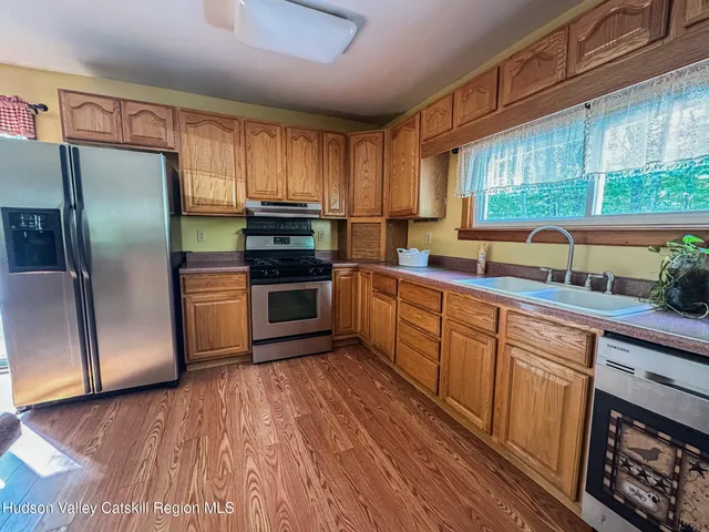 a kitchen with stainless steel appliances granite countertop a refrigerator a sink dishwasher a stove and white countertops with wooden floor