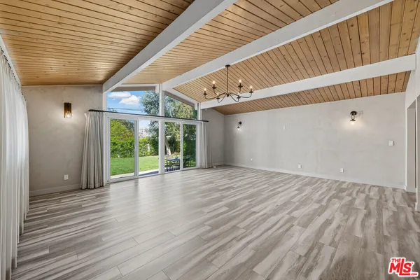 a view of an empty room with wooden floor and fan