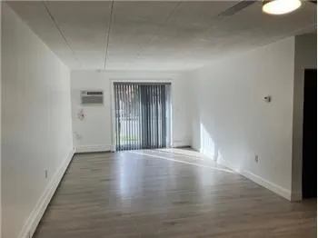 a view of an empty room with wooden floor and a window