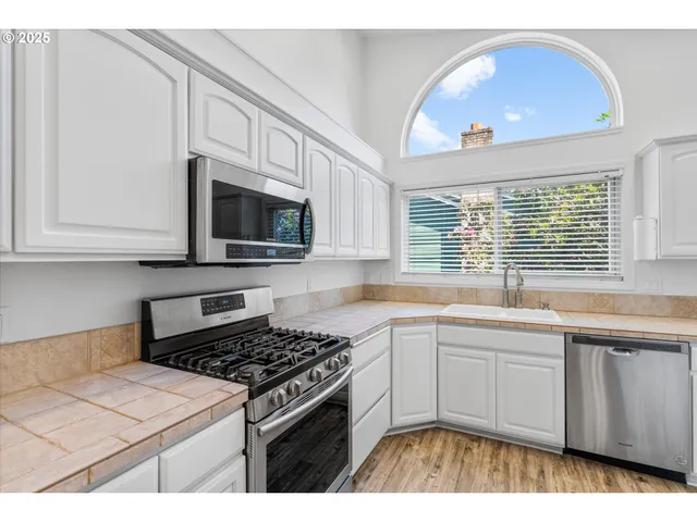 a kitchen with stainless steel appliances a sink dishwasher stove and white cabinets with wooden floor