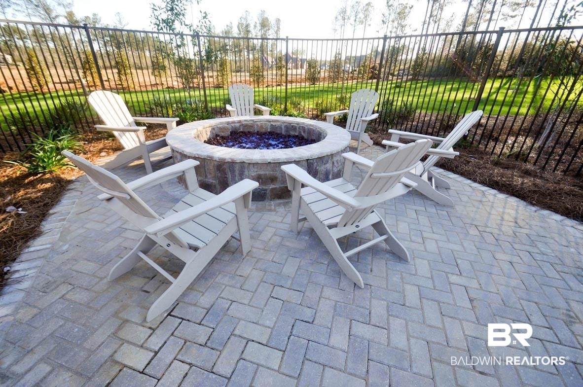 32125 Lyon Road Daphne, AL 36527 - Photo 56 of 70 Paver patio featuring a stone-clad fire pit with six Adirondack chairs, bordered by a black metal fence and landscaped areas