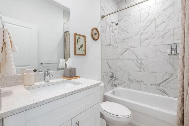 a bathroom with a granite countertop bathtub shower sink vanity mirror and toilet