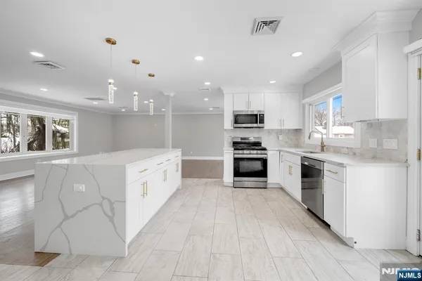 a large kitchen with a large counter top a sink stainless steel appliances and cabinets