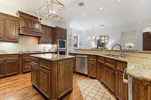 a kitchen with stainless steel appliances granite countertop a stove top oven a sink dishwasher a refrigerator and white cabinets with wooden floor