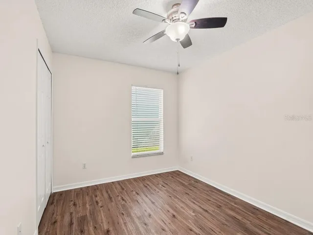 an empty room with wooden floor chandelier fan and windows