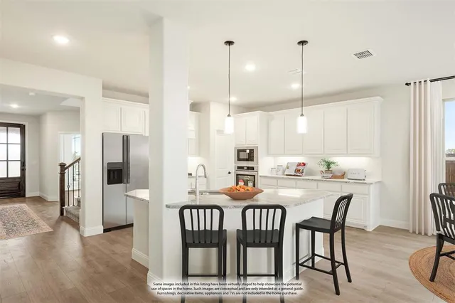 a kitchen with stainless steel appliances kitchen island granite countertop a dining table chairs and a refrigerator