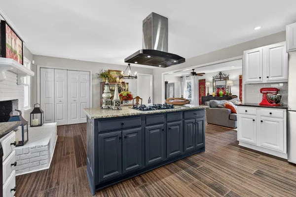 a kitchen with stainless steel appliances kitchen island granite countertop a sink dishwasher and white cabinets with wooden floor
