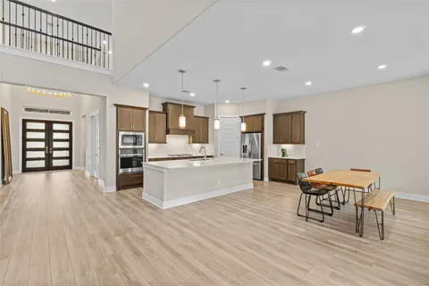 a large white kitchen with stainless steel appliances kitchen island granite countertop a stove a refrigerator a sink a dining table and chairs with wooden floor