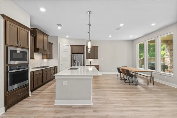 a large kitchen with stainless steel appliances kitchen island granite countertop a large stove a sink dishwasher a dining table and chairs with wooden floor