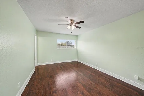 an empty room with wooden floor chandelier fan and windows