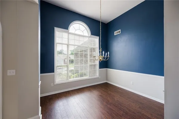 an empty room with wooden floor chandelier and windows