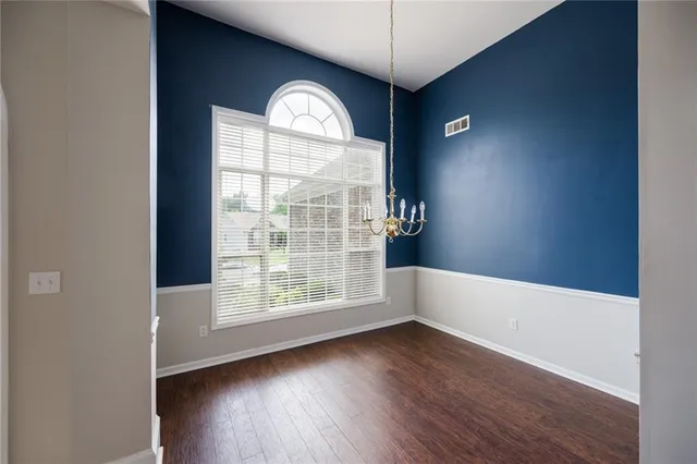 an empty room with wooden floor chandelier and windows